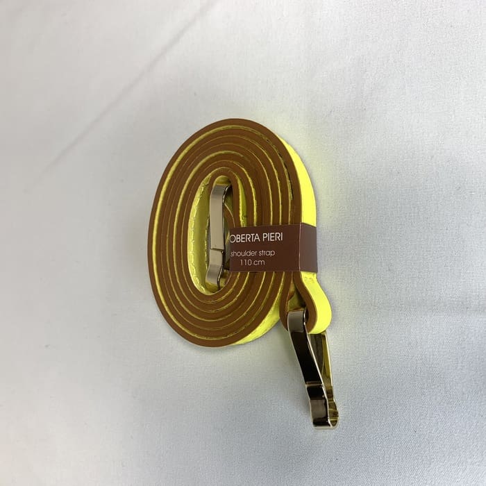 La bandoulière jaune avec garnitures dorées est enroulée et l’étiquette marron « ROBERTA PIERI bandoulière 110 cm » est ornée sur la surface blanche.