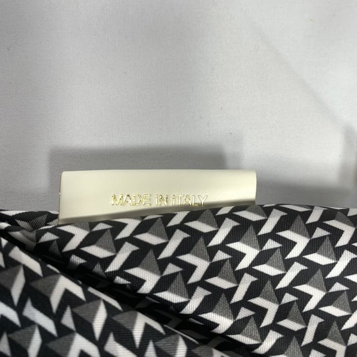 Le tissu géométrique noir et blanc du mini duffel ROBERTA PIERI avec une étiquette blanche sur laquelle on peut lire « MADE IN ITALY » en lettres dorées. L’arrière-plan est blanc uni.