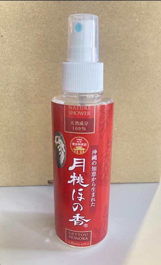 Un vaporisateur rouge avec les mots « Nature Shower » écrits sur un fond beige. Buse et capuchon de pulvérisation blancs.