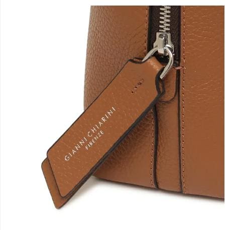 Gros plan sur le sac en cuir marron de GIANNI CHIARINI. Il est doté d’une fermeture éclair en métal et d’une étiquette en cuir sur laquelle on peut lire « GIANNI CHIARINI FIRENZE » en blanc. Il est fabriqué en Italie et respire l’élégance italienne intemporelle.